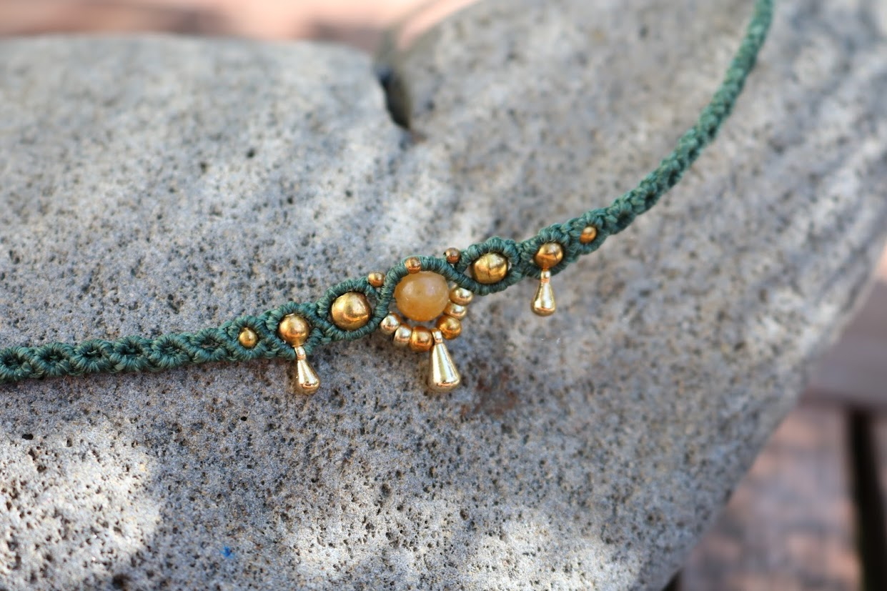 Green macrame necklace with gold beads on a stone surface