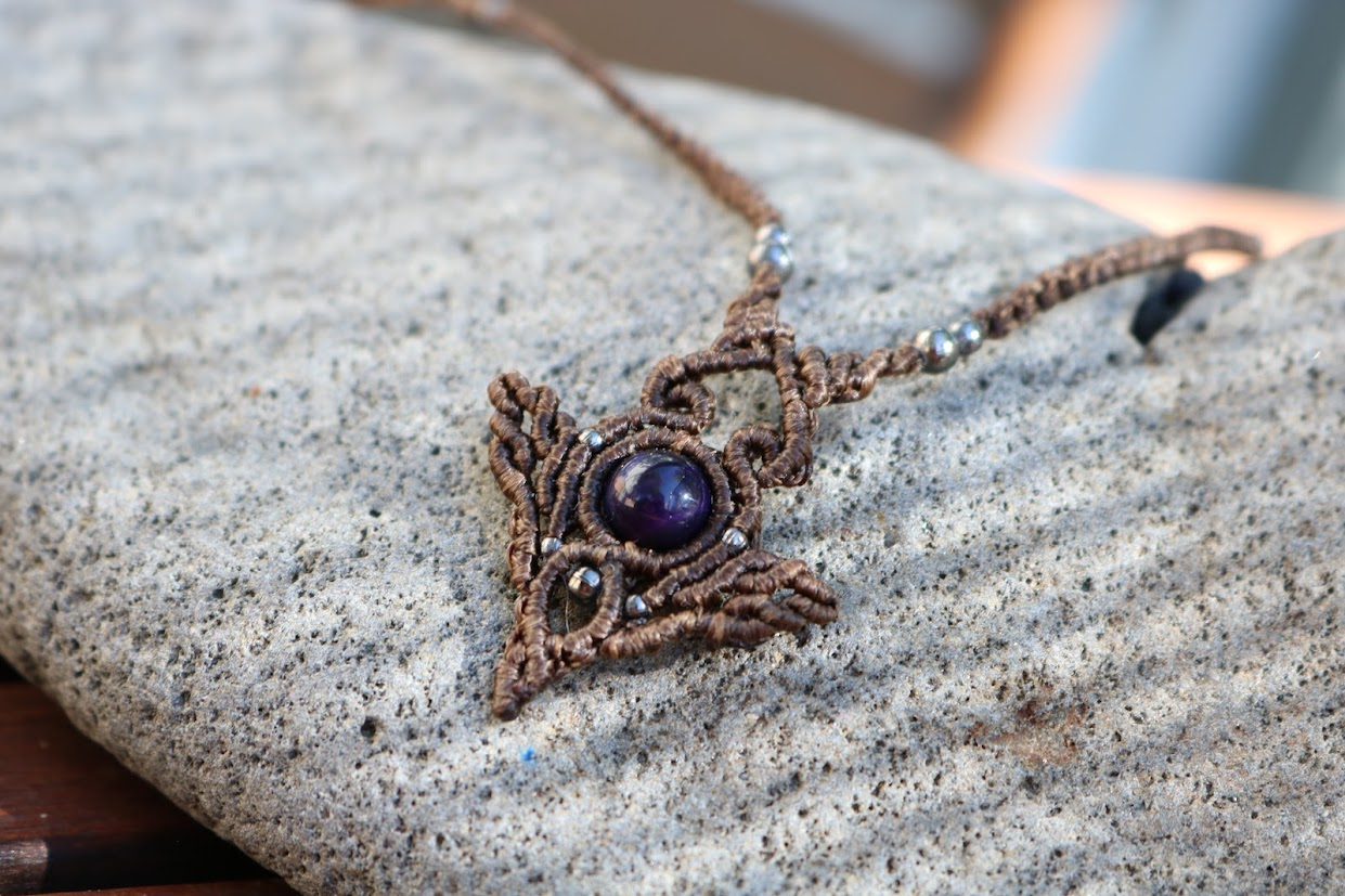 Necklace with a decorative pendant featuring a purple gemstone on a stone surface.