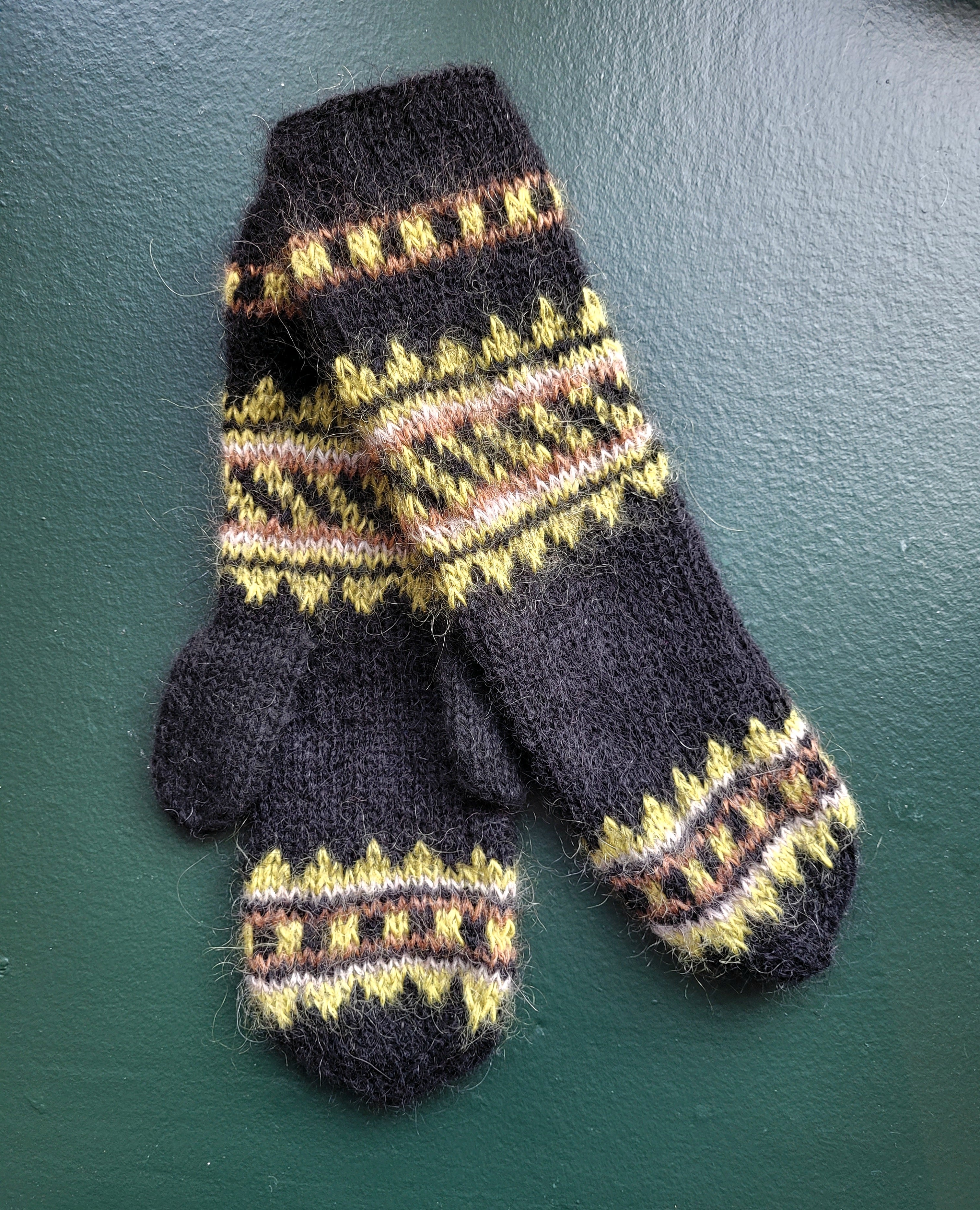 Knitted black mittens with a green pattern on a dark green background