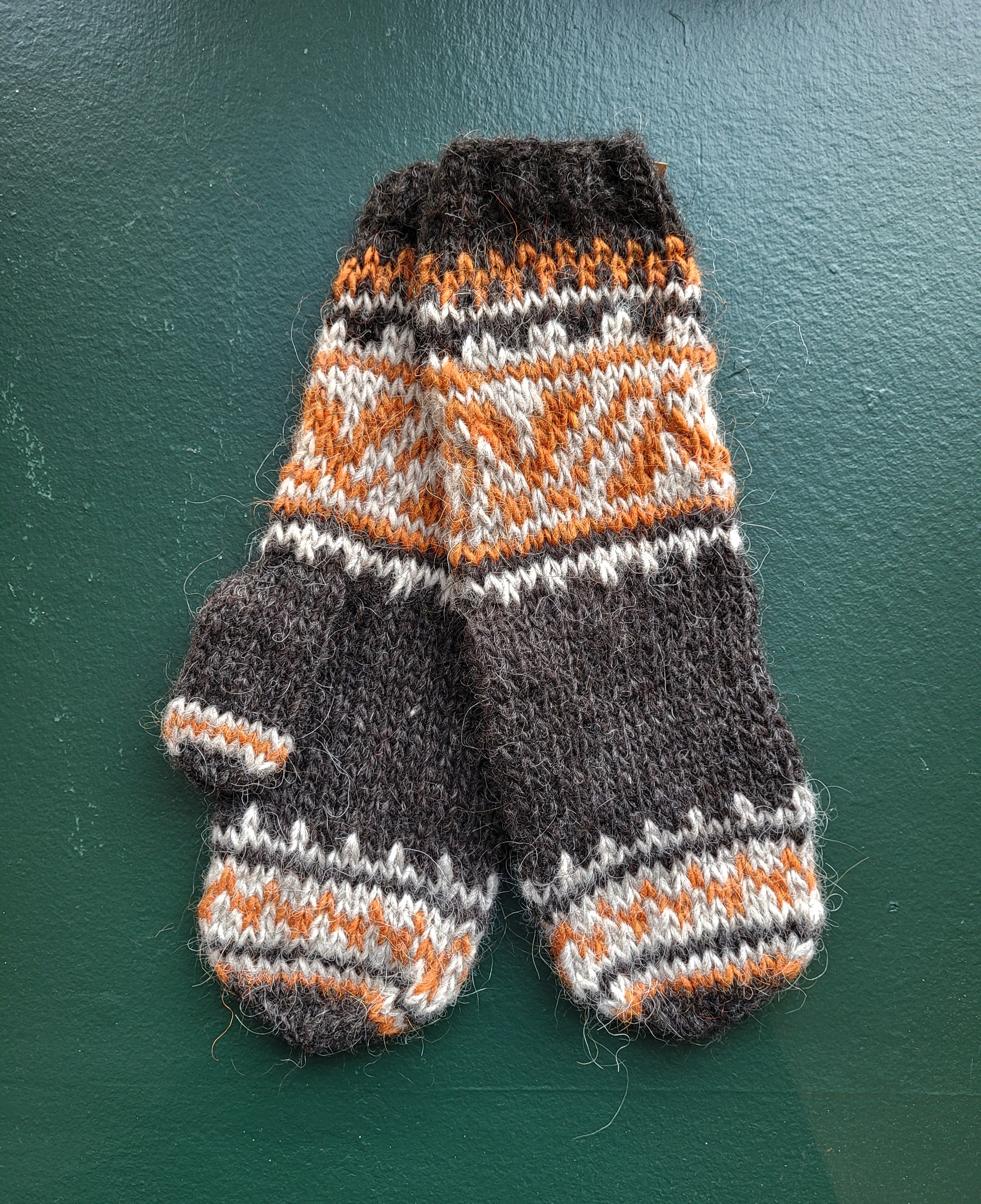 Pair of knitted mittens with a geometric pattern on a green background