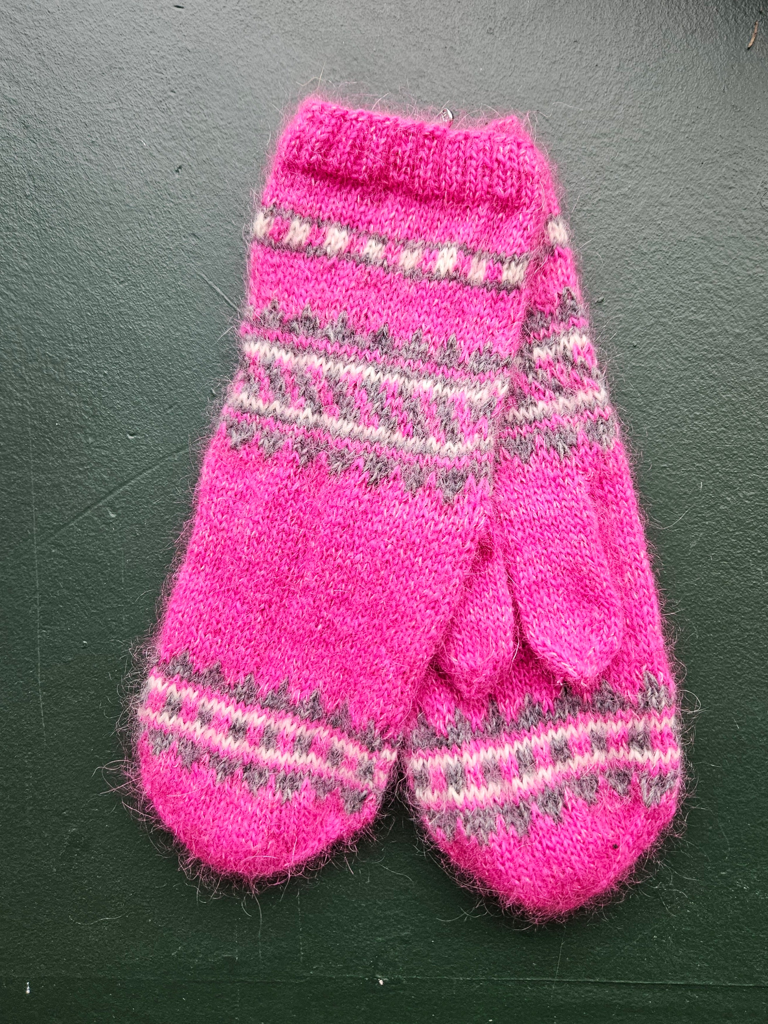 Pair of pink knitted mittens with a pattern on a dark surface