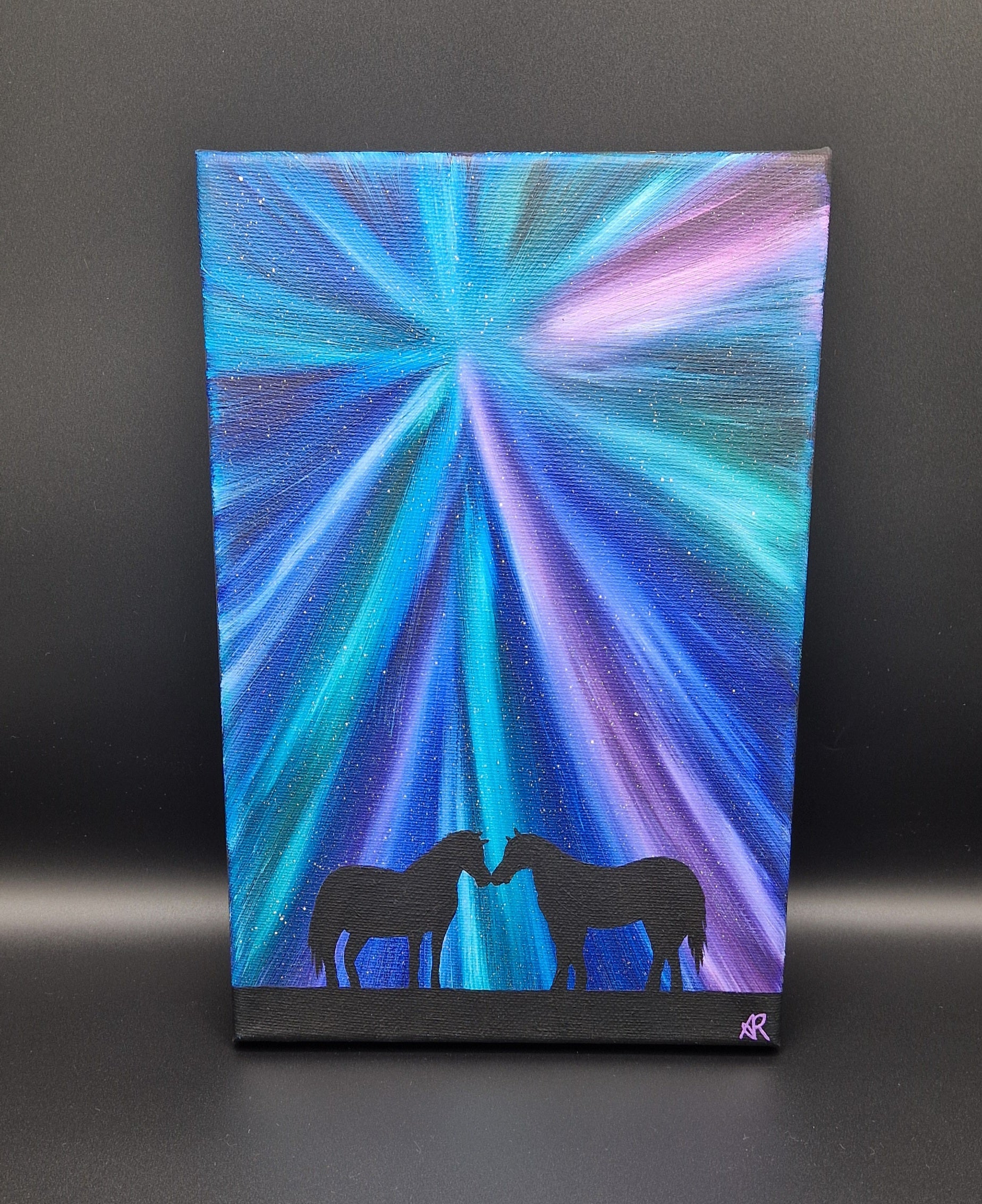 Canvas painting with a starburst northern lights design and horse silhouettes on a dark background