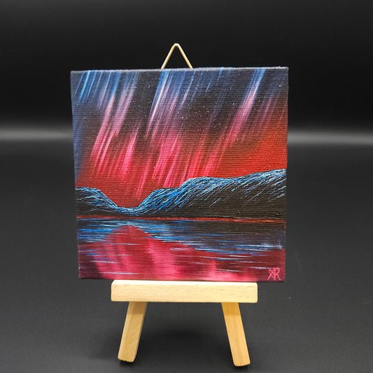 Northern lights landscape painting featuring blue and red northern lights over mountains reflected in water.