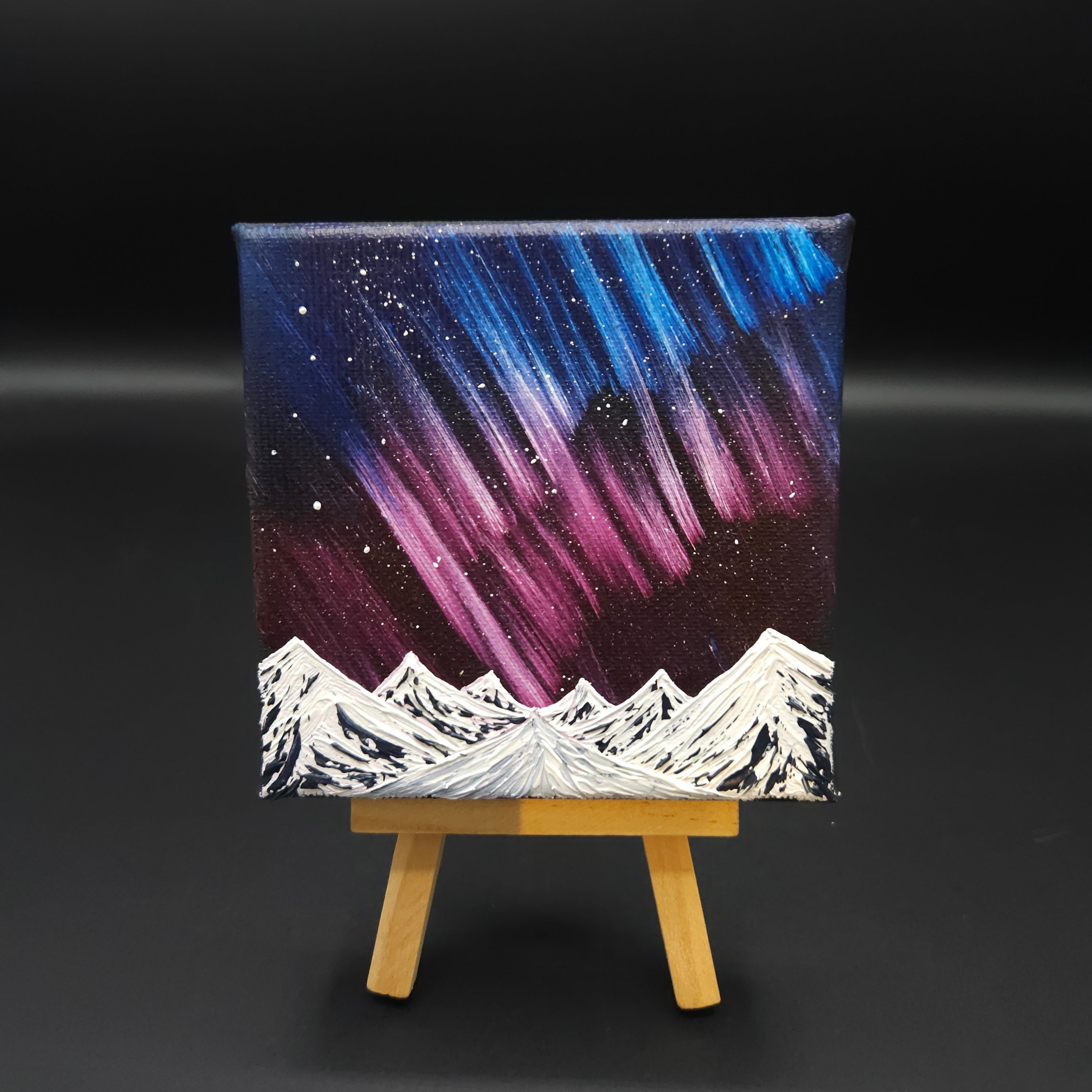 Northern lights landscape painting featuring blue and red northern lights over snow-capped mountains.