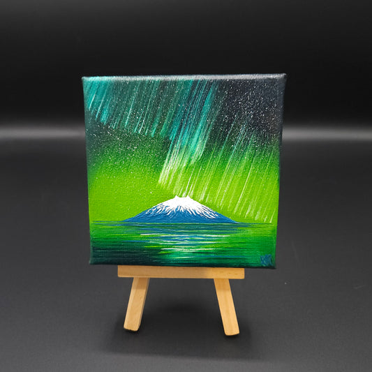 Northern lights landscape painting featuring blue and green northern lights over a snow-capped mountain reflected in water.