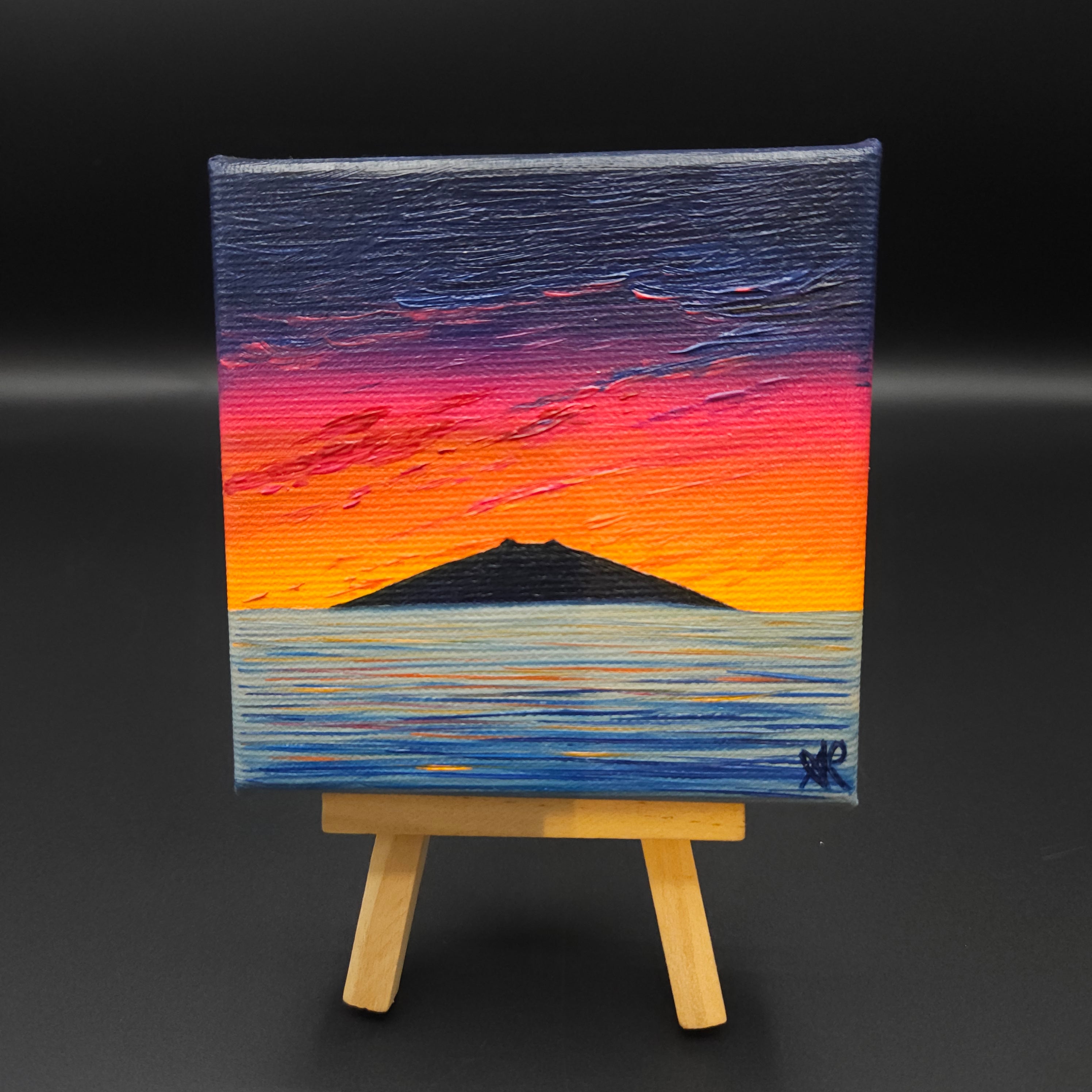 Landscape painting featuring a blue, red and orange sky and a mountain reflected in water.
