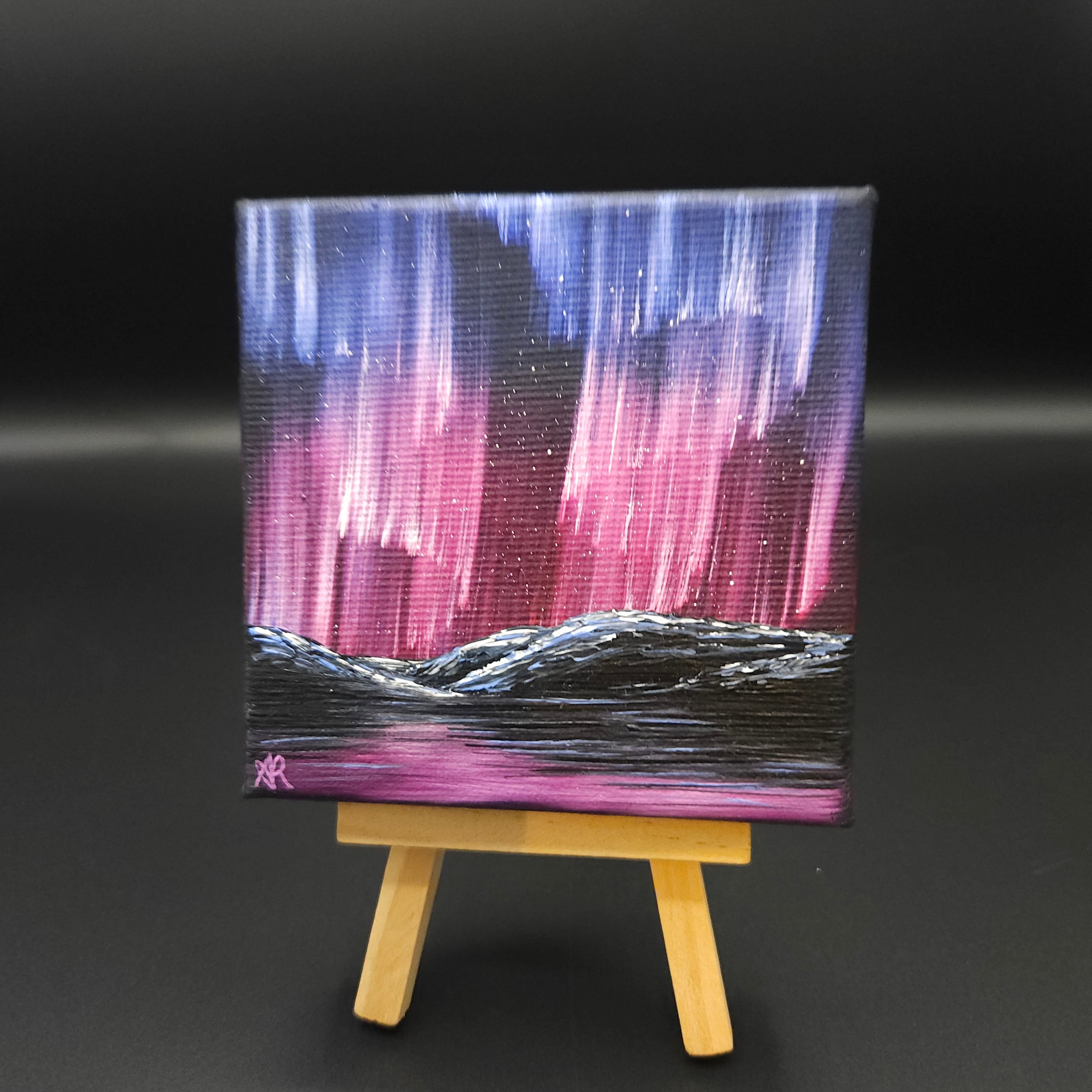 Northern lights landscape painting featuring purple and red northern lights over snow-capped mountains reflected in water.