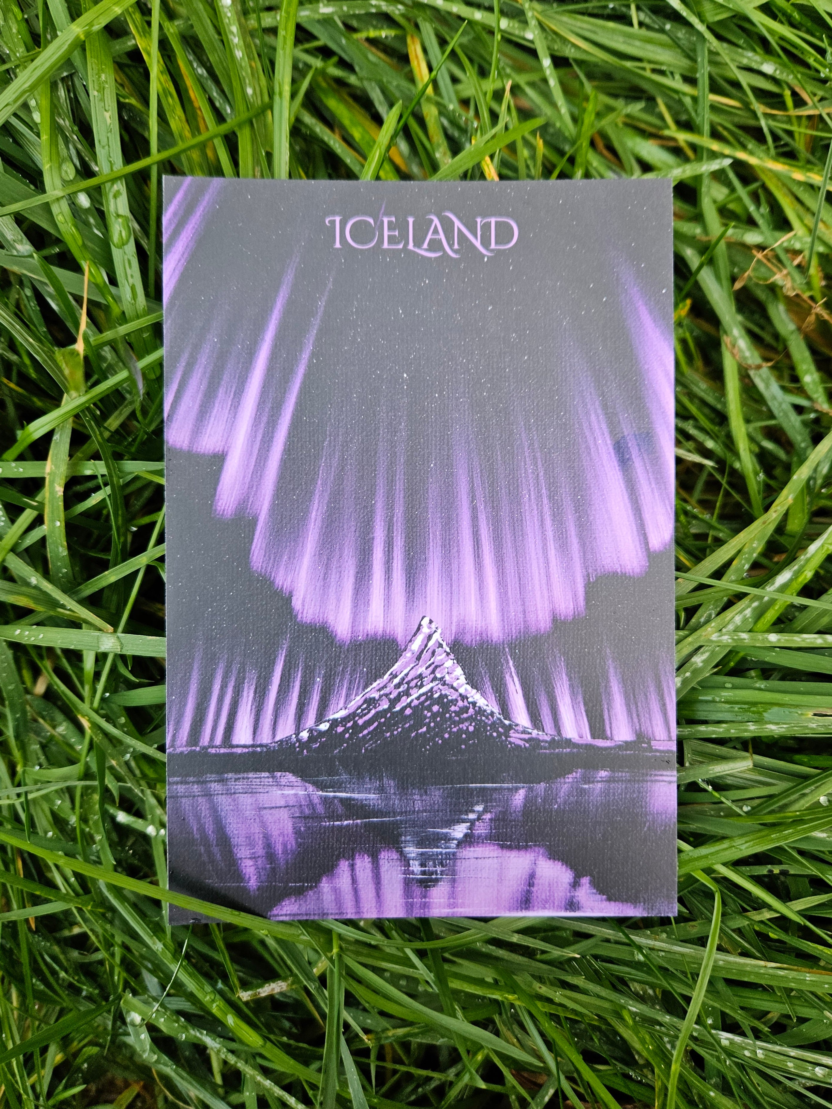 Postcard with a purple and gray design of a mountain and text 'ICELAND' on grass.
