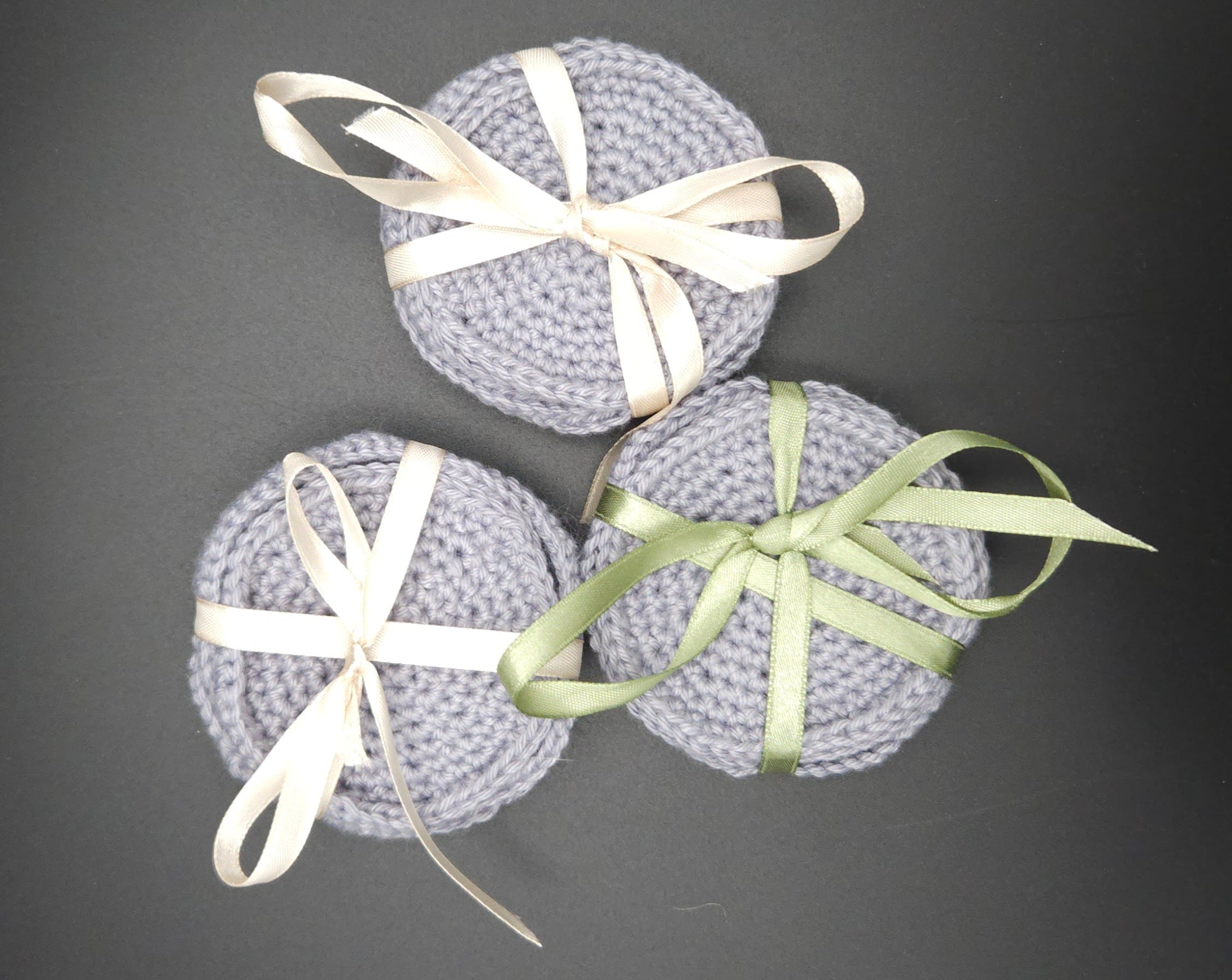 Three gray crocheted pads with ribbons on a dark background