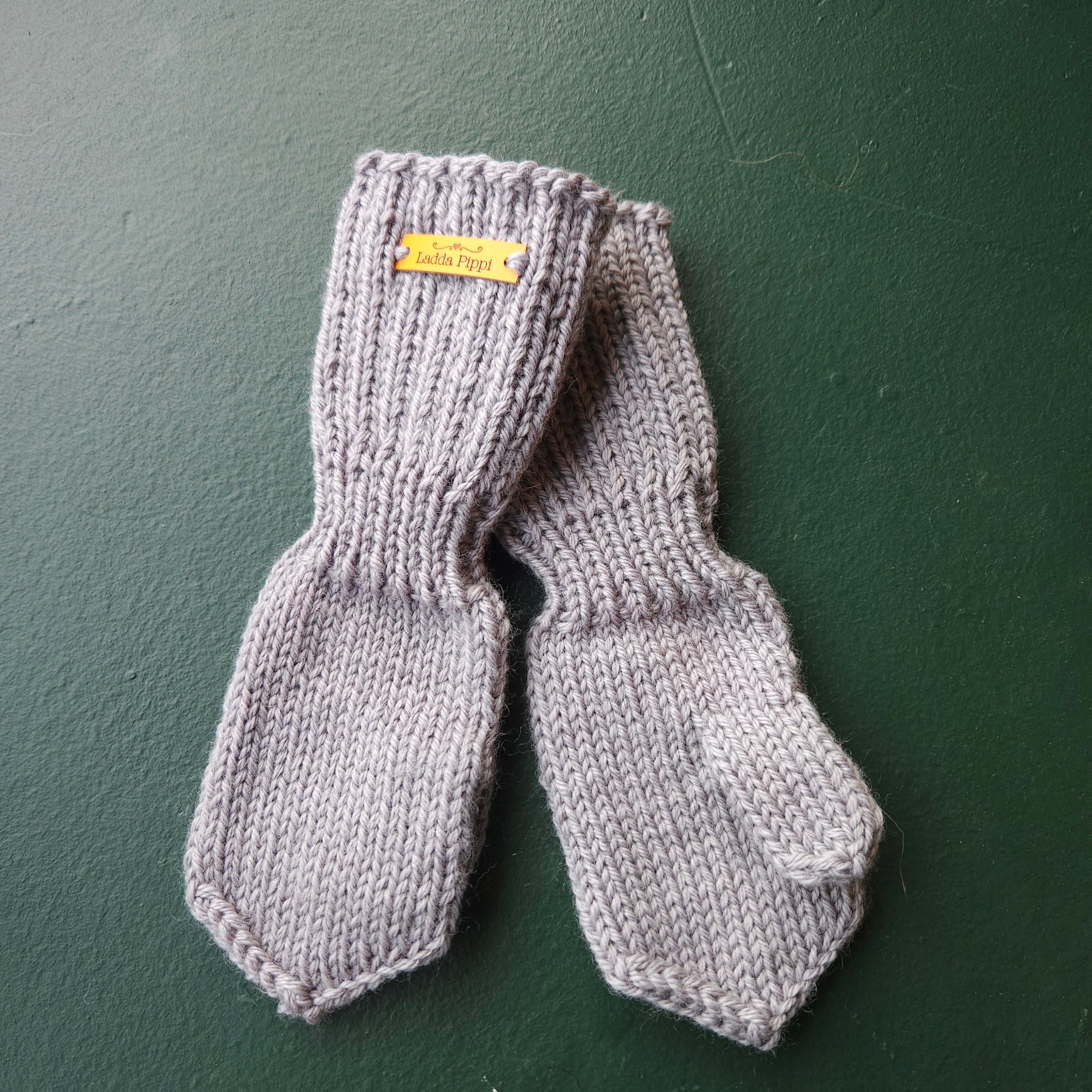 Pair of gray knit mittens with a yellow label on a green background