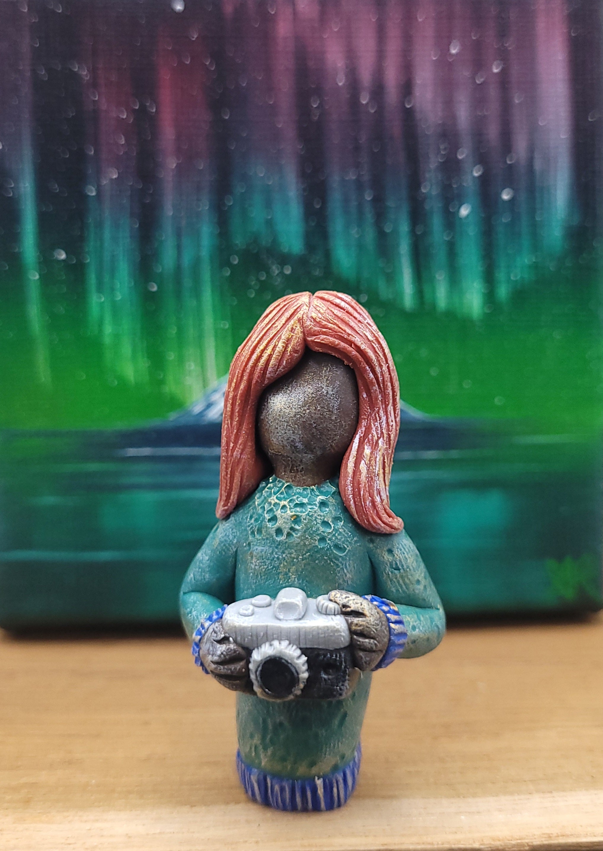 Small figurine of a person with red hair holding a camera against a colorful, abstract background