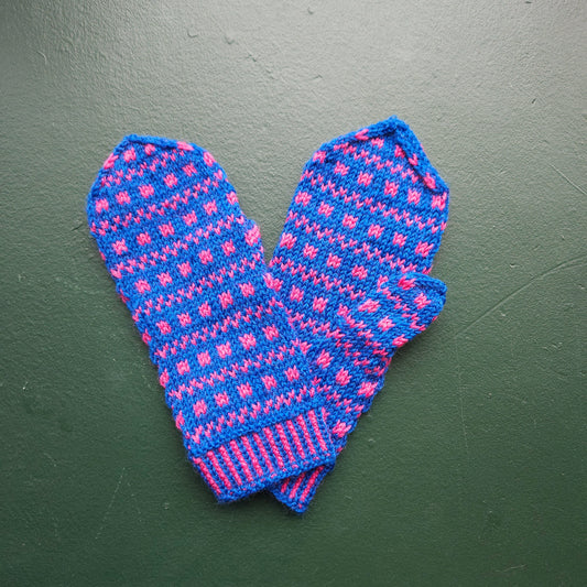 Pair of blue and pink knitted mittens on a green surface