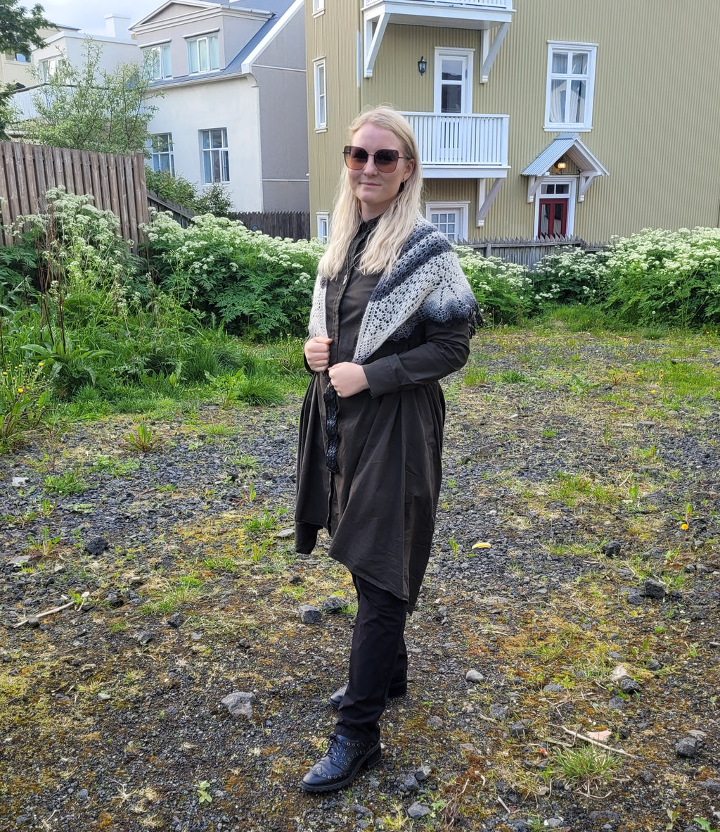 Woman standing outdoors in a residential area wearing sunglasses and a patterned shawl.