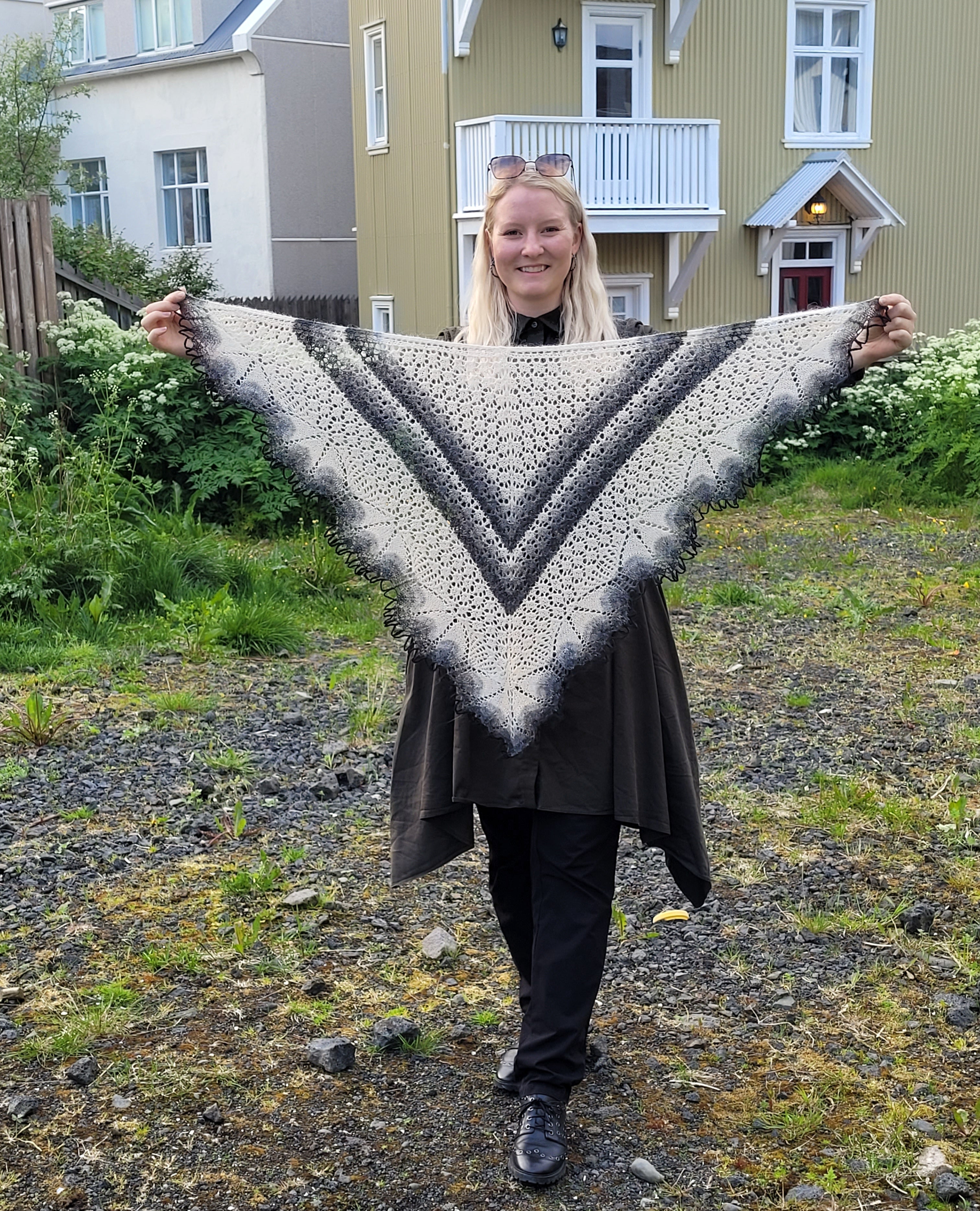 Person holding a large knitted shawl outdoors with houses in the background