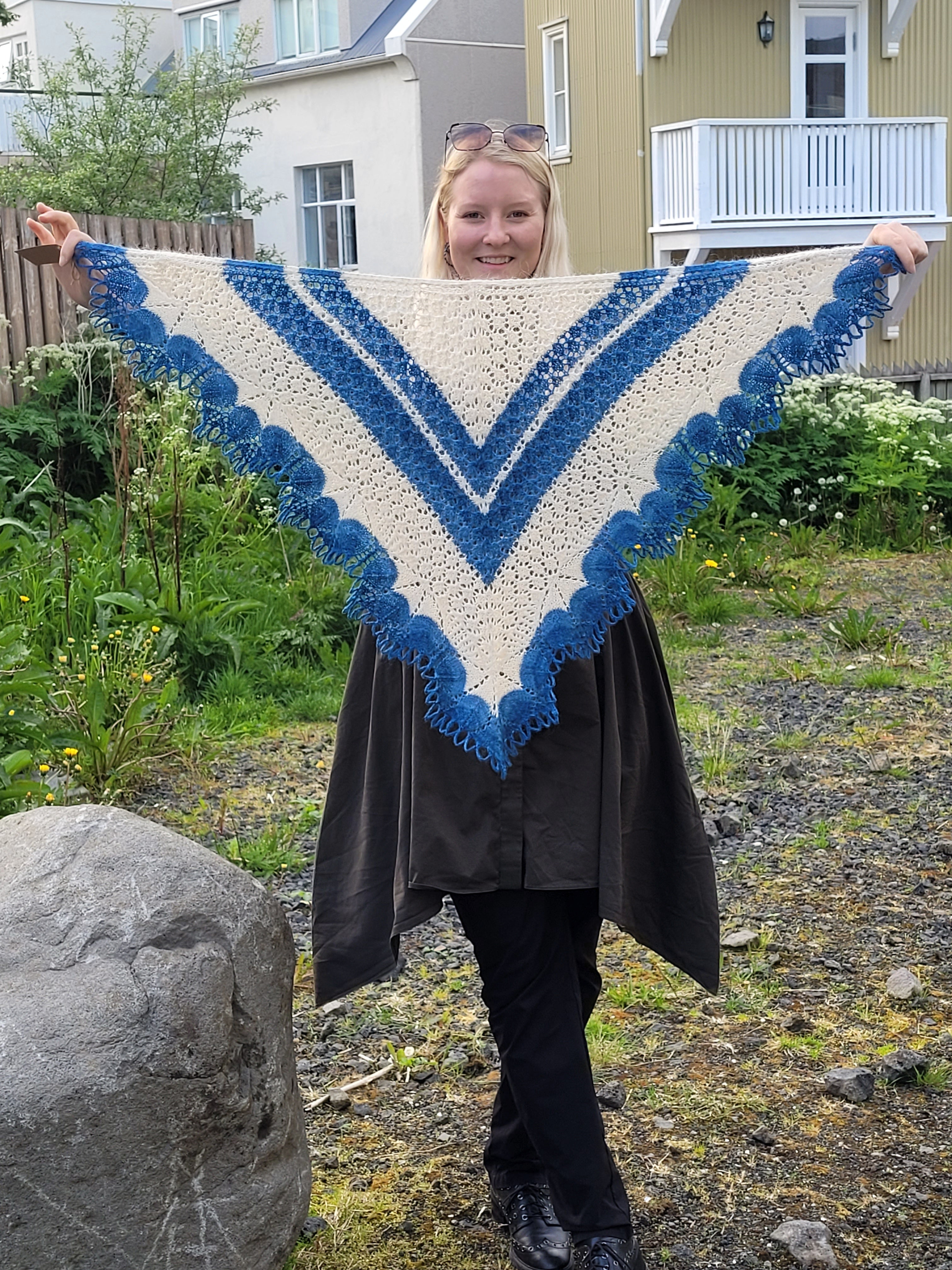 Person holding a blue and white hand-knit shawl outdoors.