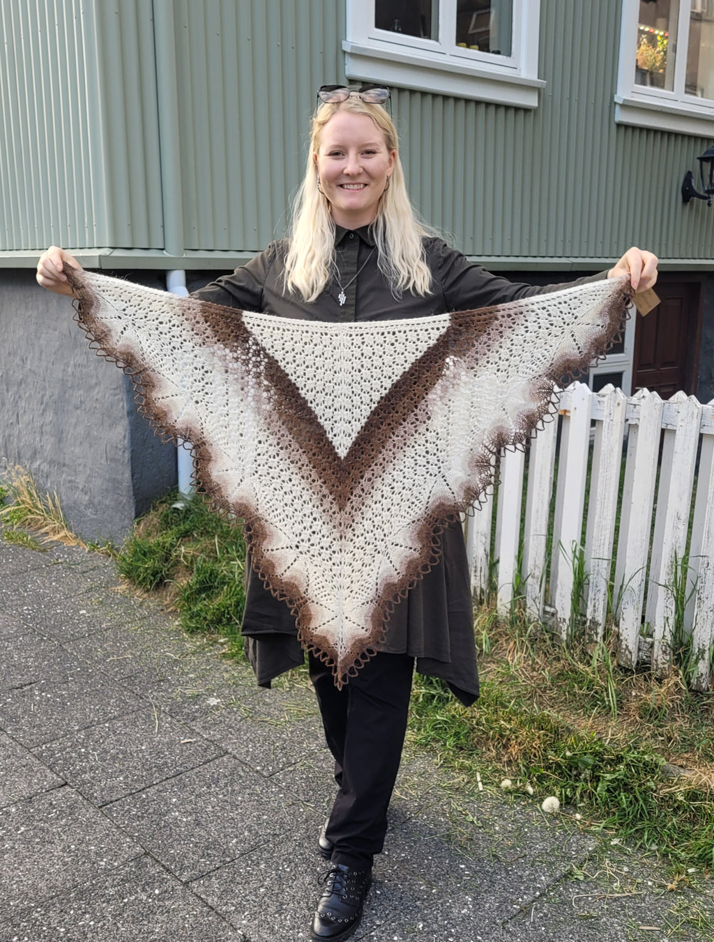 Person holding a large, triangular, brown and white knitted shawl outdoors.