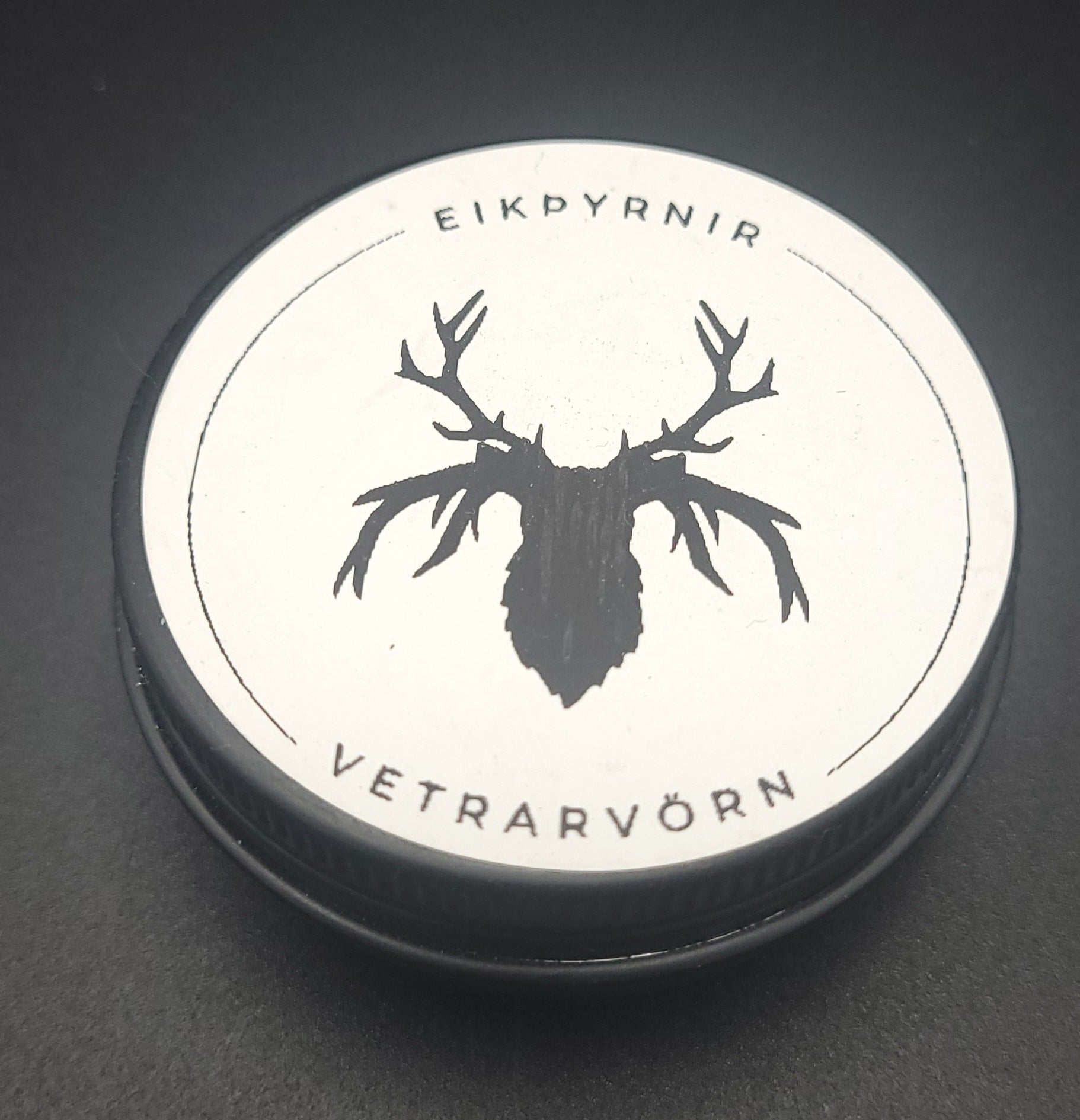 Round container lid with deer silhouette design and text on a dark background