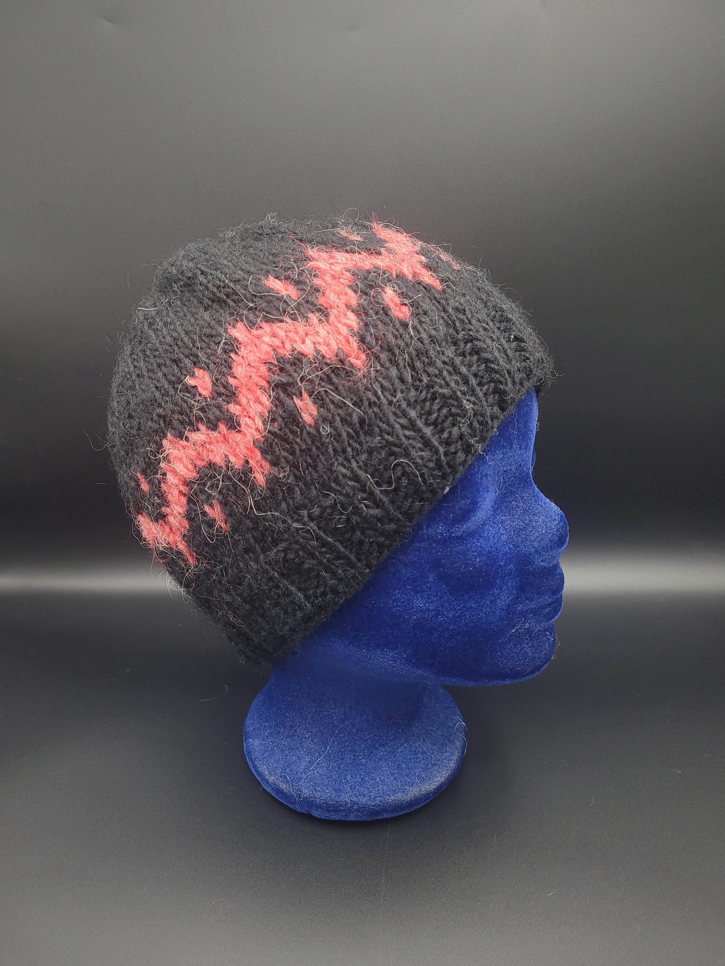 Black knitted hat with pink pattern on a blue mannequin head.