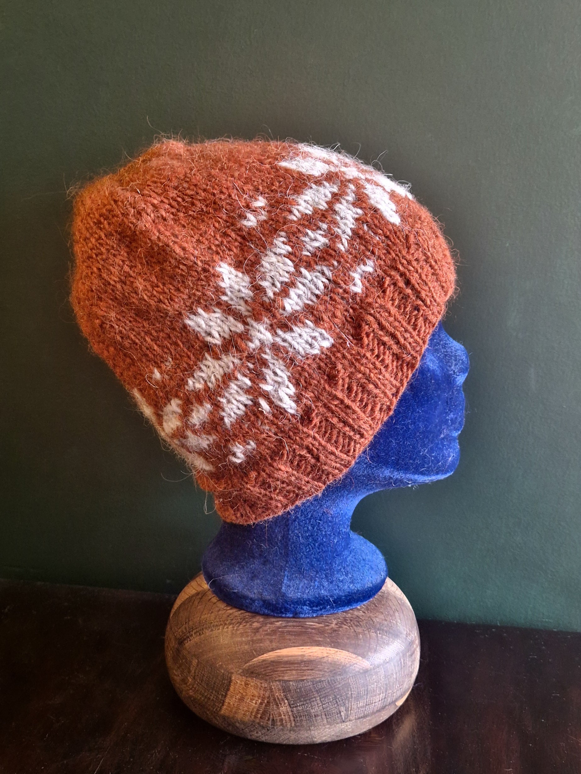 A knitted hat with a geometric pattern in red and white, displayed on a mannequin head.