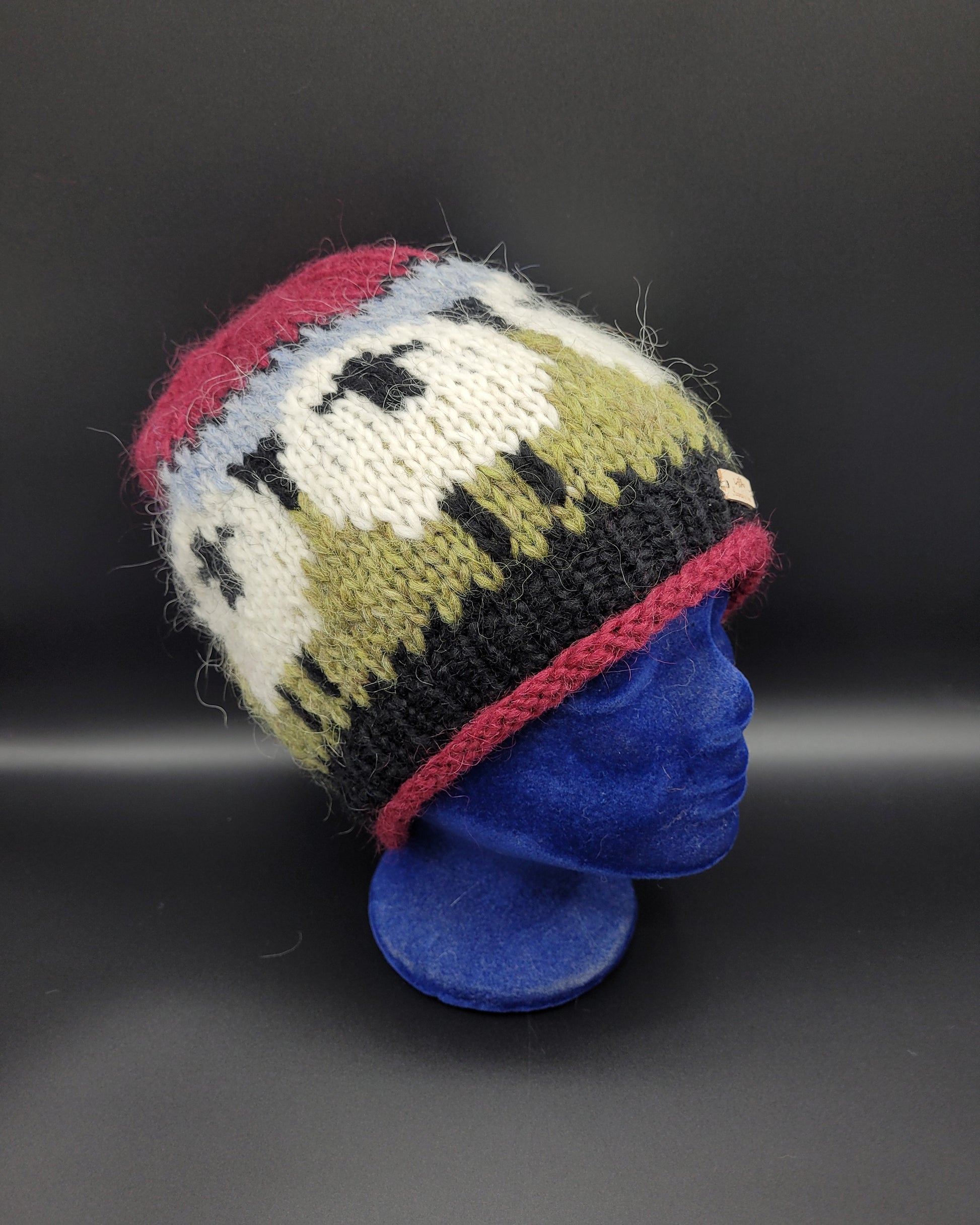 Knitted hat with sheep design on a blue mannequin head against a black background