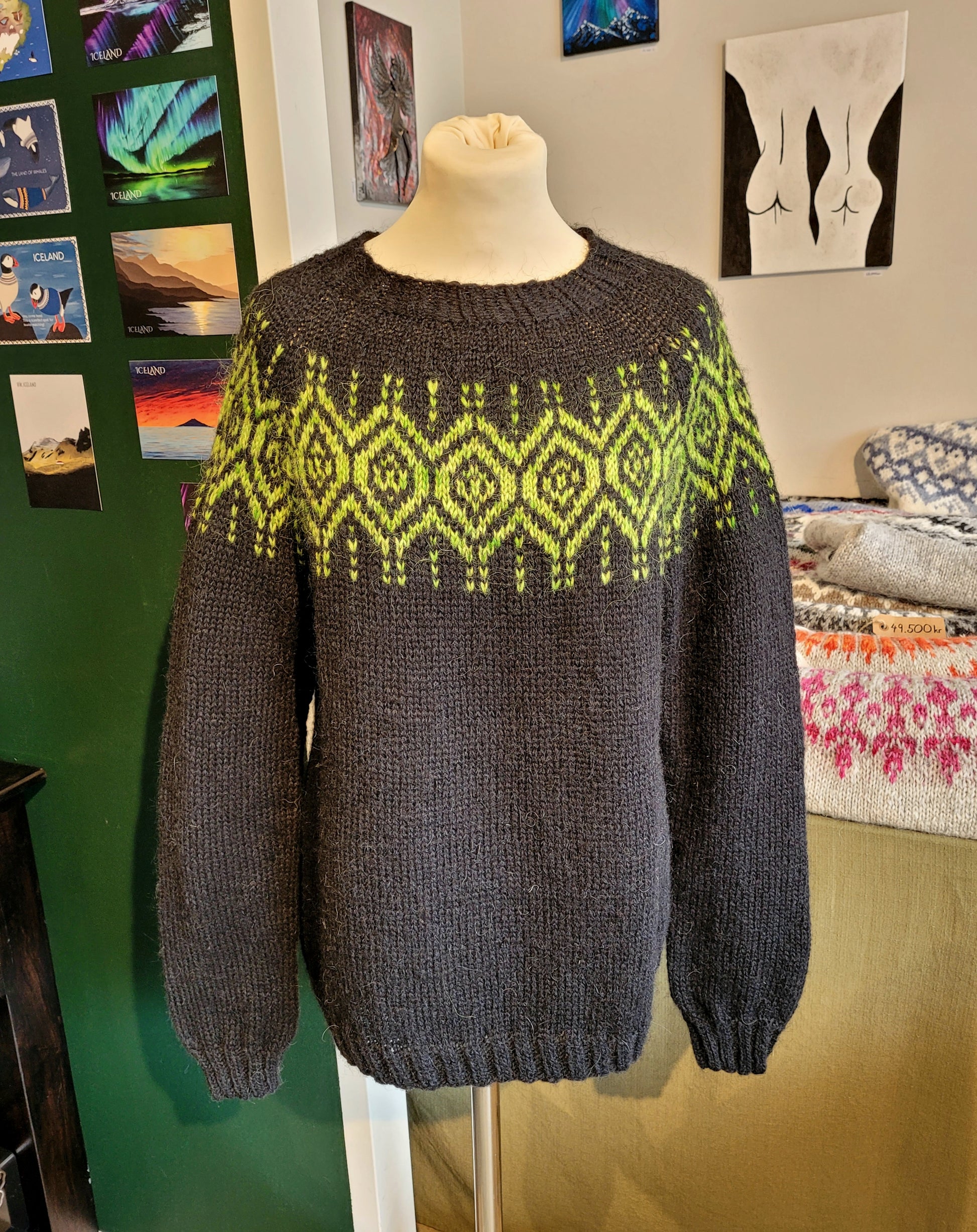 Black sweater with green pattern on a mannequin against a colorful wall.