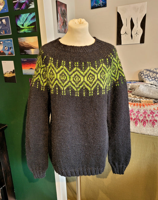 Black sweater with green pattern on a mannequin against a colorful wall.